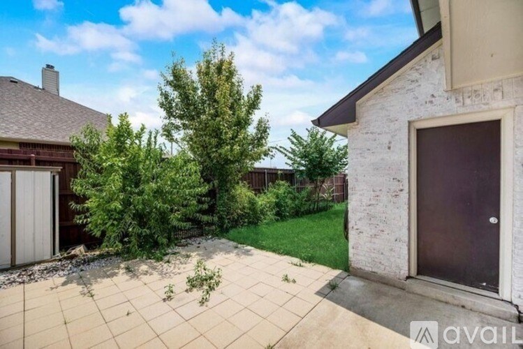 A backyard with a tree, a patio, and a house.