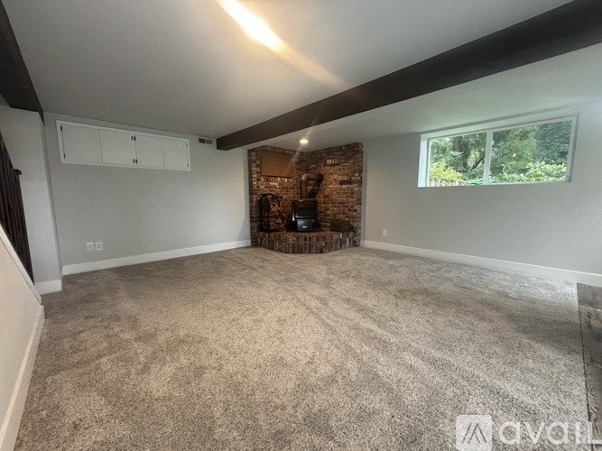 A room with a carpeted floor and a window showing greenery outside.