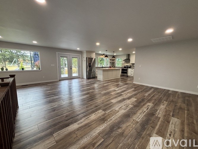 A spacious room with wooden flooring and a kitchen area in the background.