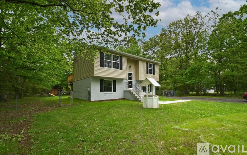 A house with a white and beige exterior is surrounded by greenery.