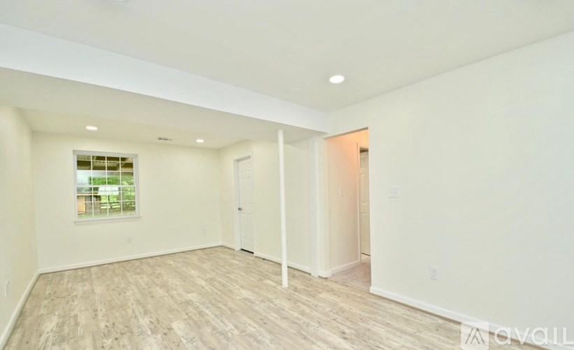 A spacious room with light wood flooring and white walls.