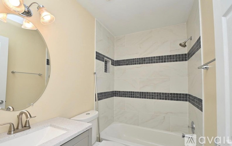A bathroom with a white sink, a round mirror, and a shower with black and white tiles.