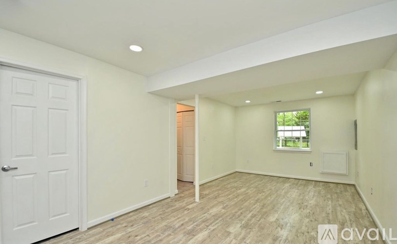 A room with a white door and a window with a view of a tree and a bench outside.