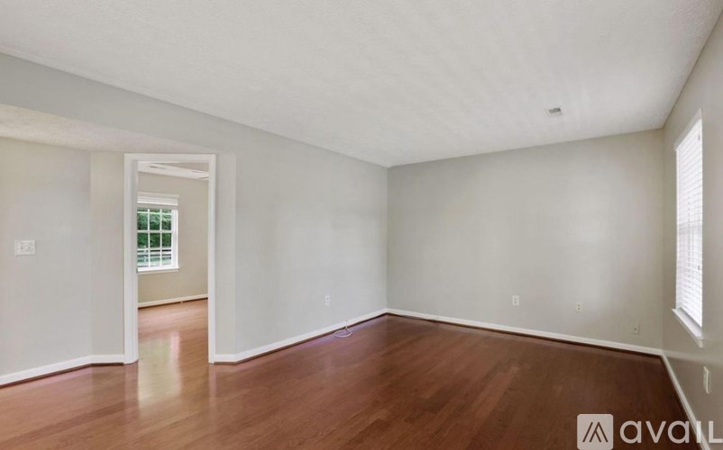 A room with wooden floors and white walls, with a doorway leading to another room.