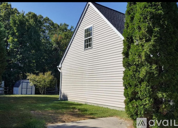 A small house with a grey siding is surrounded by greenery.