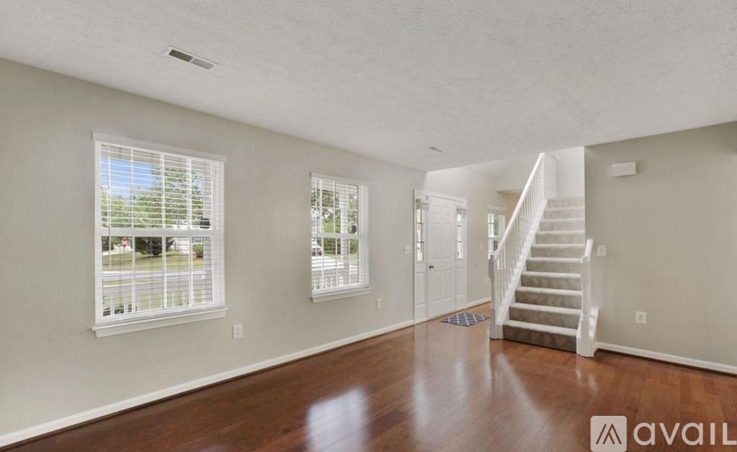 A spacious room with wooden floors and a staircase leading to another room.