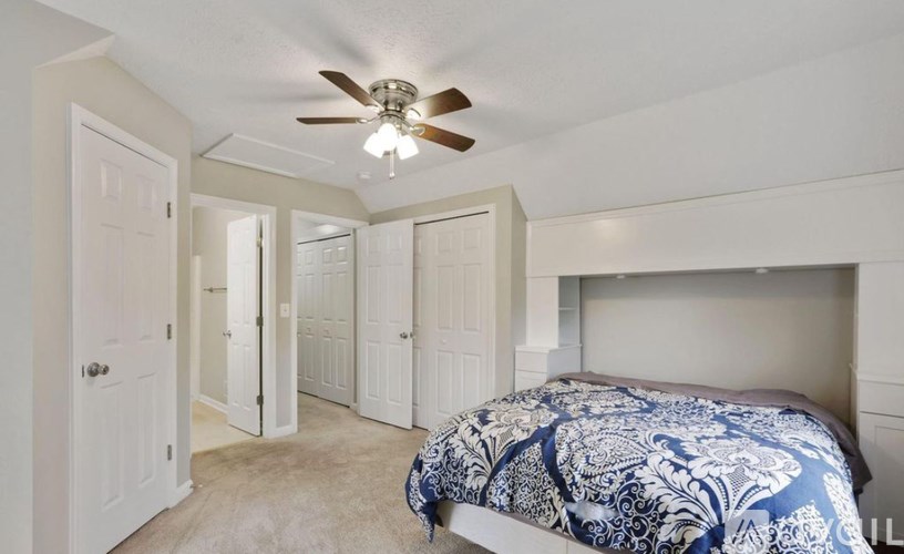 A bedroom with a bed, a ceiling fan, and a doorway leading to another room.