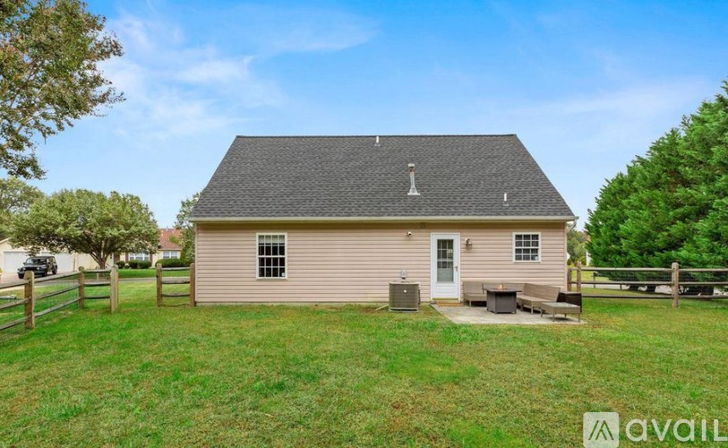 A small house with a brown roof and a white door is surrounded by a grassy area and trees.