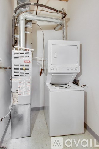 A white tank sits next to a white box with pipes running along the wall.