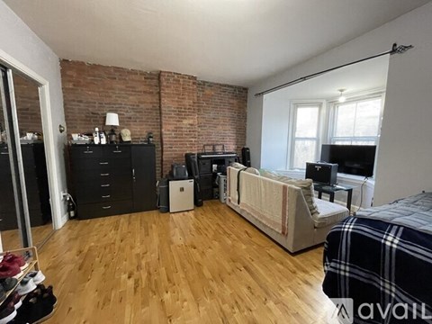 A bedroom with a bed, dresser, and a brick wall.