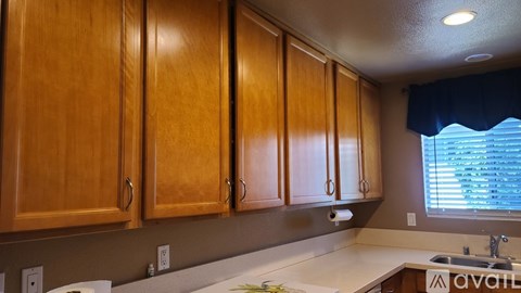 A kitchen with wooden cabinets and a window with blinds.