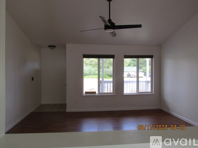Empty room with a ceiling fan and two windows.