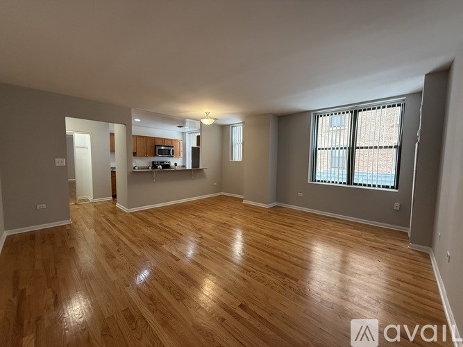 A spacious room with wooden flooring and a window with blinds.