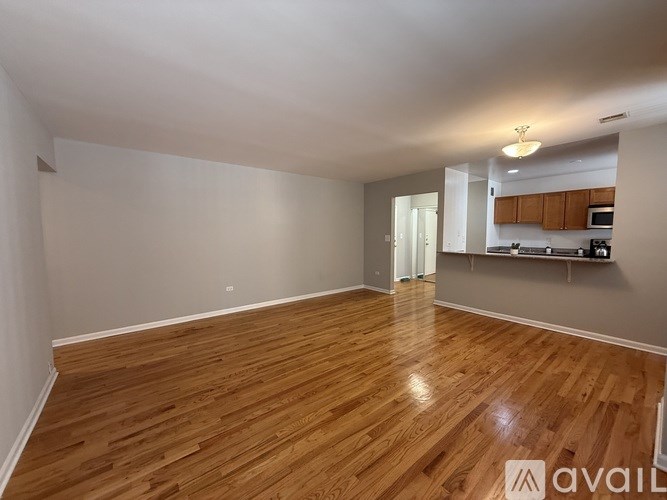 A spacious room with wooden flooring and a kitchen area in the background.