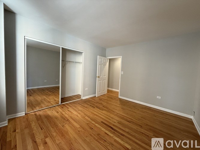 A room with wooden floors and white walls, with a large mirror on the left side.