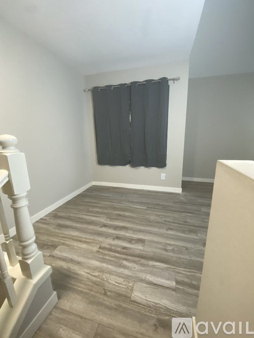 A room with wooden flooring and a staircase on the left side.