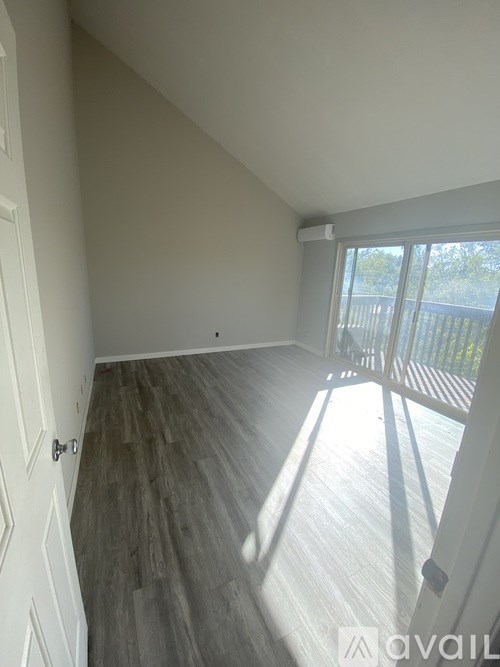 A room with wooden flooring and a sliding glass door leading to a balcony.