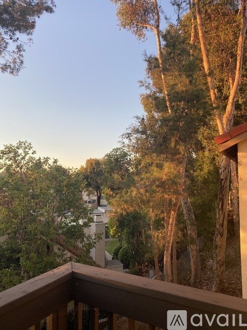 A balcony overlooks a forest with a house in the distance.
