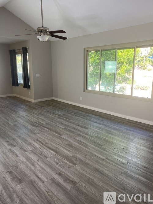A room with a ceiling fan and a window with a view of trees.