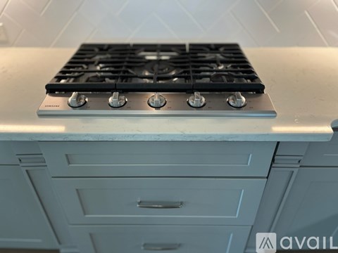 A black gas stove with four burners is installed in a kitchen with white cabinets.