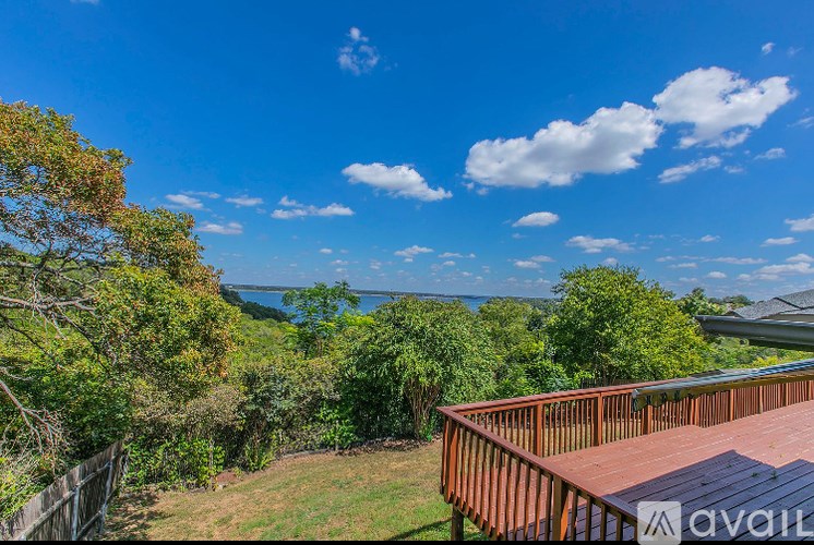 A wooden deck overlooks a lush green landscape and a body of water under a blue sky.