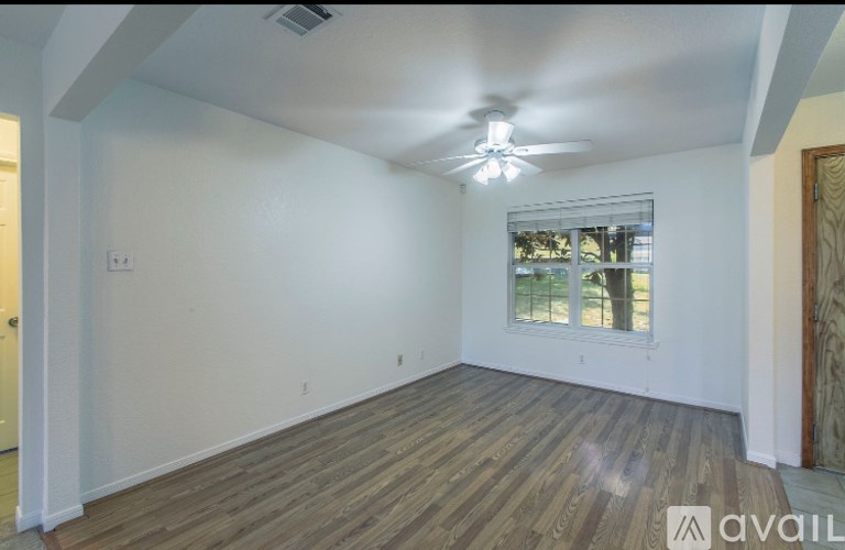A room with wooden flooring and a window with a view of trees.