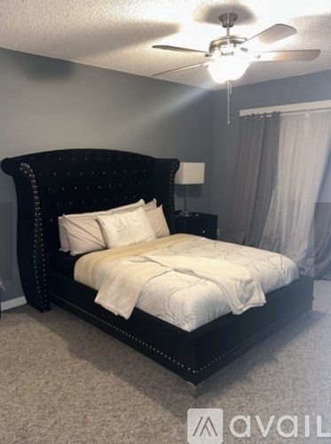 A bedroom with a black bed and a ceiling fan.