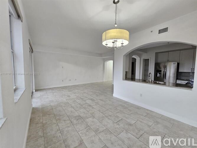 A spacious room with a chandelier and a kitchen in the background.
