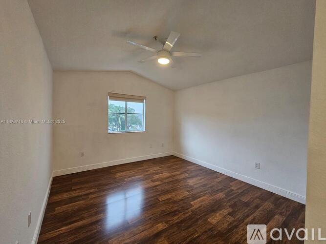 A spacious room with wooden flooring and a ceiling fan.