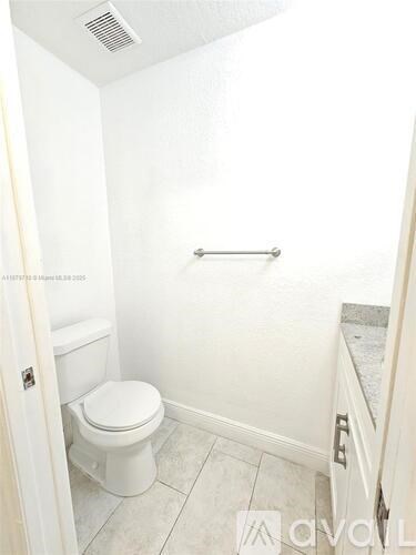 A white toilet in a small bathroom with a white wall and a white door.