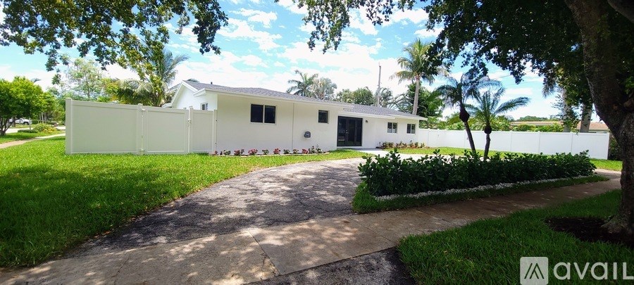 A white house with a driveway and trees in front.