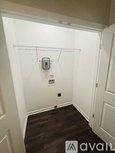 A small room with a white door and a white wall with a small electrical outlet and a small white shelf.