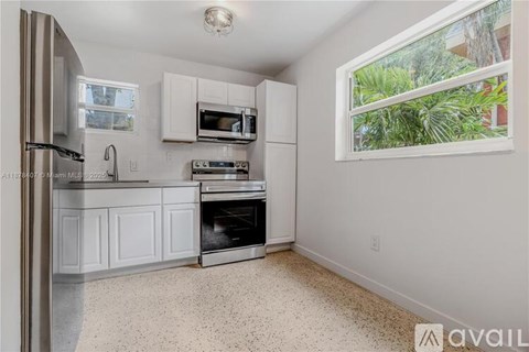 A kitchen with white cabinets and appliances, a window, and a tiled floor.