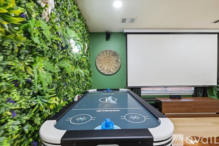 A shiny green plant wall behind a table with a screen on it.
