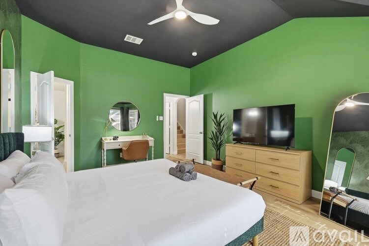 A bedroom with a white bed, a green wall, and a television.