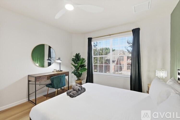 A bedroom with a large bed, a desk with a mirror, and a window with black curtains.