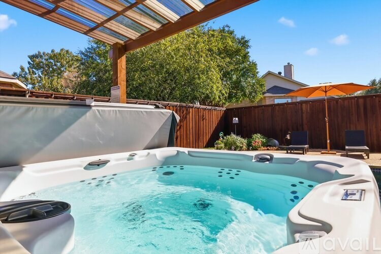 A hot tub is in the middle of a backyard with a wooden fence and trees in the background.