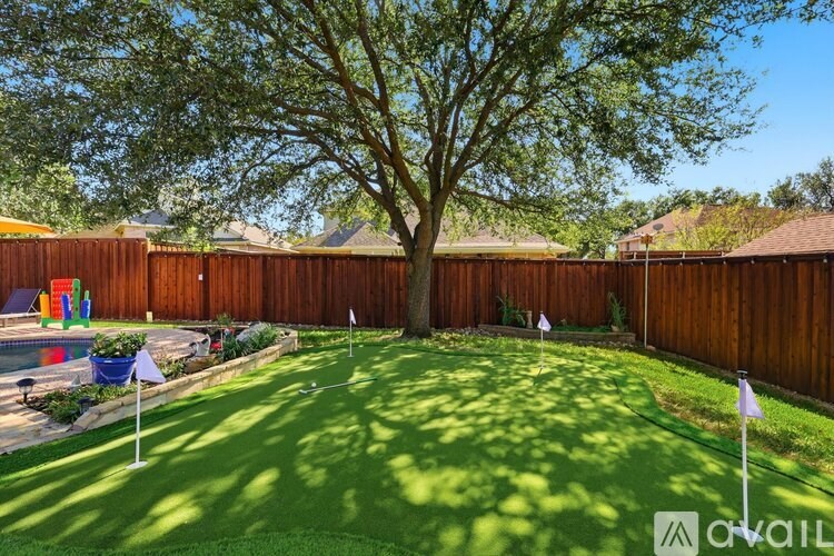 A backyard with a green lawn and a large tree in the middle.