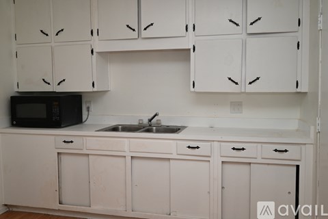 A kitchen with white cabinets and a black microwave.