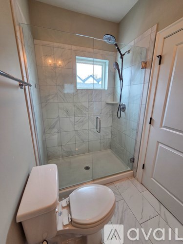 A bathroom with a toilet, a glass shower stall, and a window.