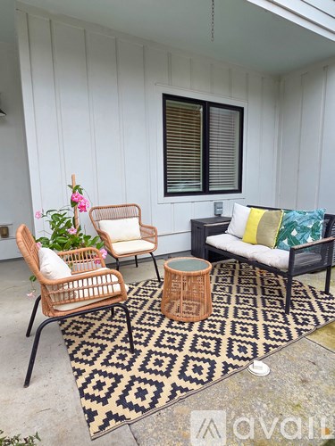 A patio with a wicker chair, a sofa, and a table with a vase of flowers on it.