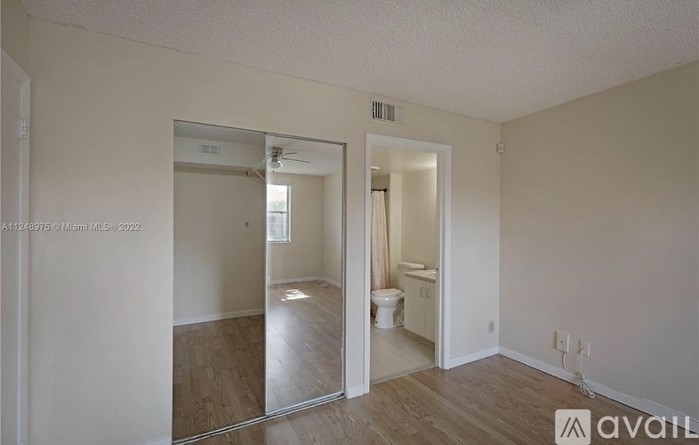 A room with a mirrored door and a toilet in the other room.