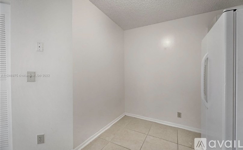 A white refrigerator is in the corner of a small, empty room.