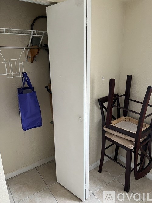 A chair with a wooden frame and beige cushion sits in a room with a white door.