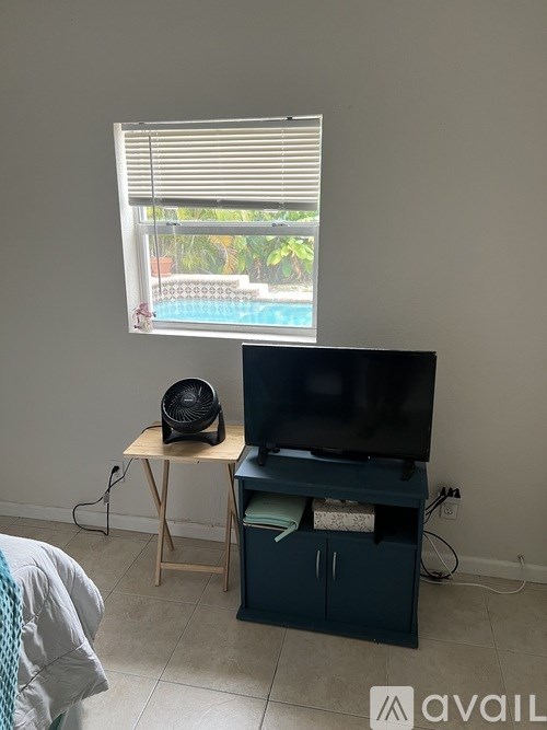 A room with a television, a fan, and a window overlooking a pool.