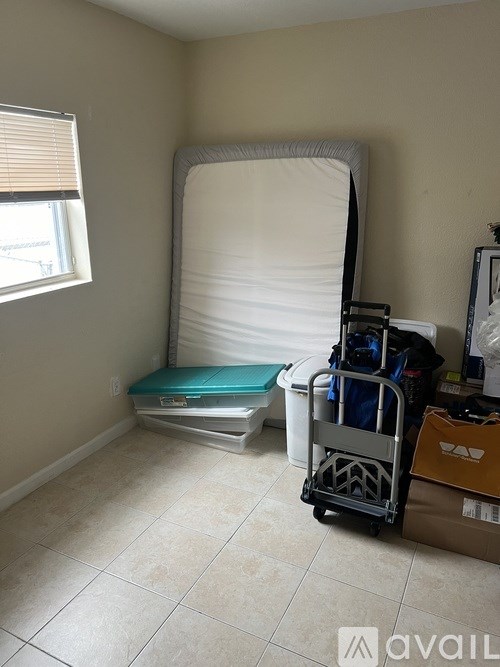 A room with a white bed and a window with blinds.