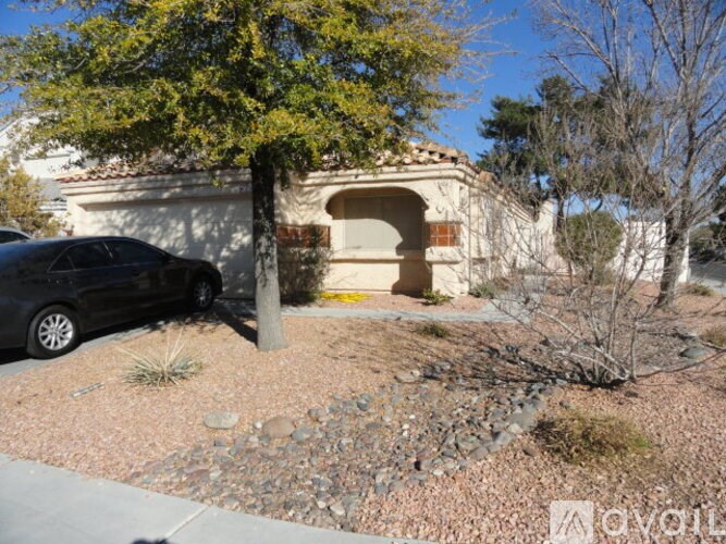 A black car is parked in front of a house with a tree and a bush.