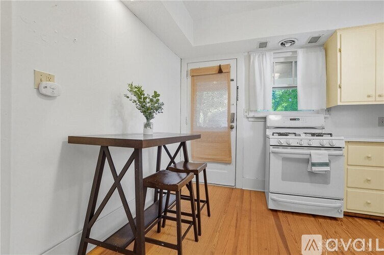 A kitchen with a wooden table and chairs, a white oven, and a window with a view of trees.
