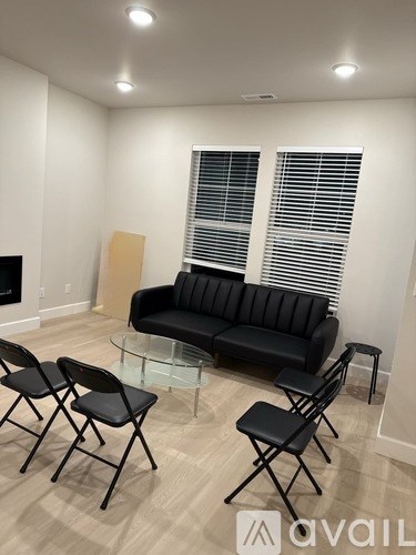 A living room with a black sofa, glass coffee table, and three black chairs.