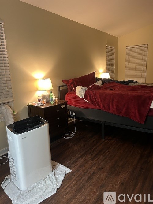 A bedroom with a red bed, a white air conditioner, and a wooden floor.